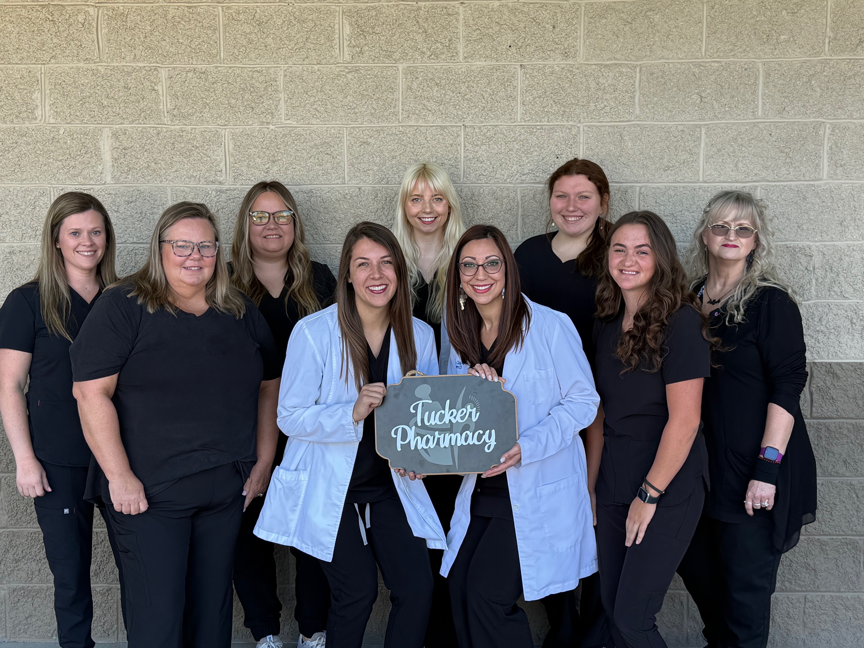 The Tucker Pharmacy team gathered together holding a Tucker Pharmacy sign